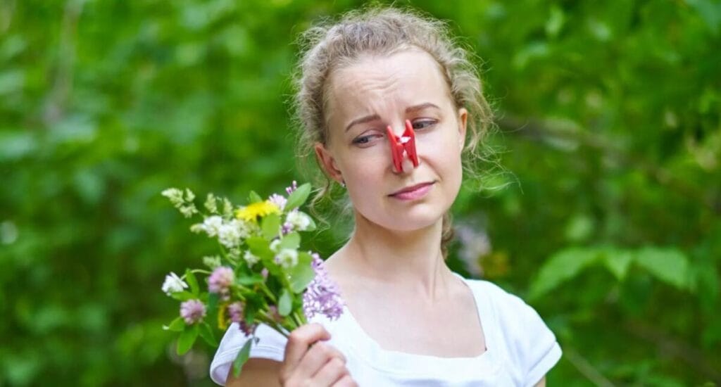 девушка чихает на улице в маске на фоне цветущих деревьев.