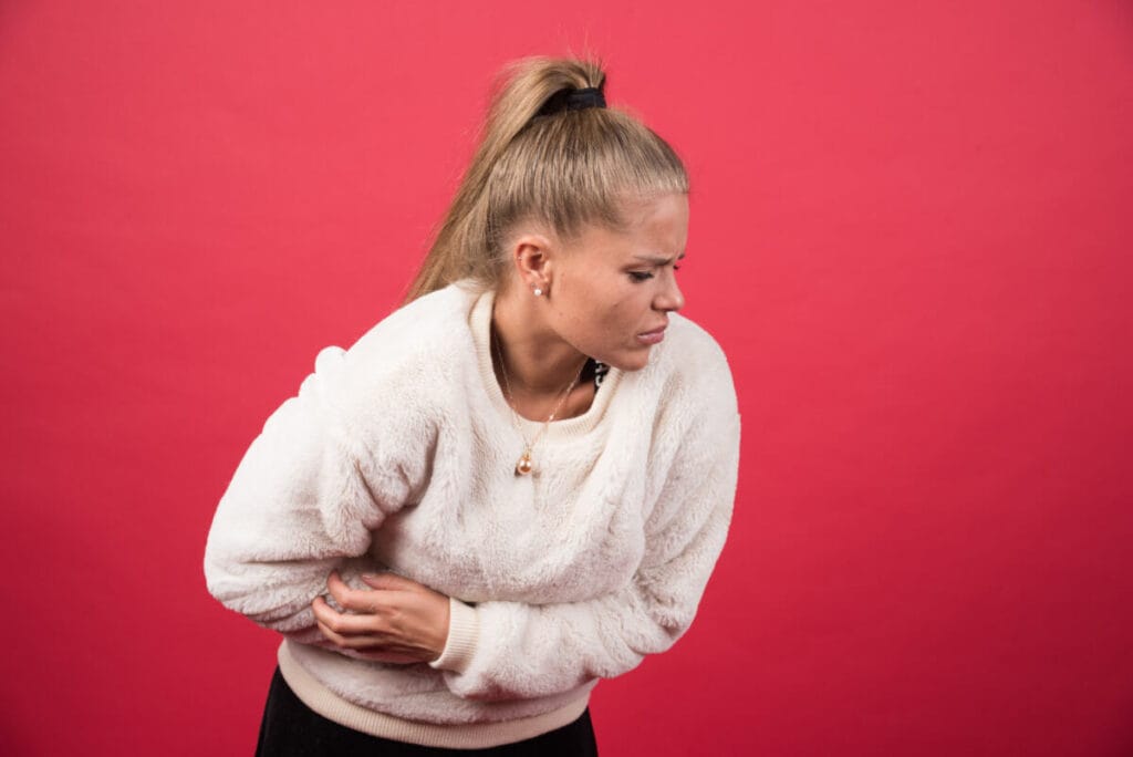 woman sitting with hand on stomach, feeling discomfort