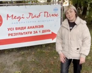 Жінка вказує на рекламний банер медичної лабораторії Меді Лаб Плюс біля Хмельницької районної лікарні на Львівському шосе